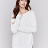 Ecru white long-sleeved knit sweater with lace-up cuffs, rounded hem, and front pockets by Charlie B.