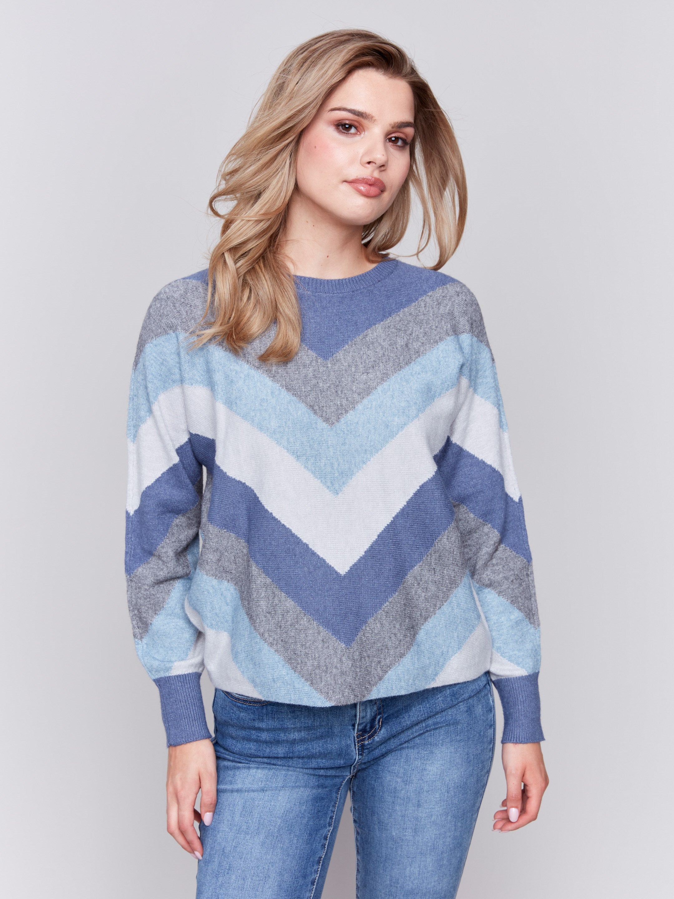 Denim-colored long-sleeve sweater with chevron stripes in blue, grey, and white. Crew neckline and ribbed cuffs by Charlie B.