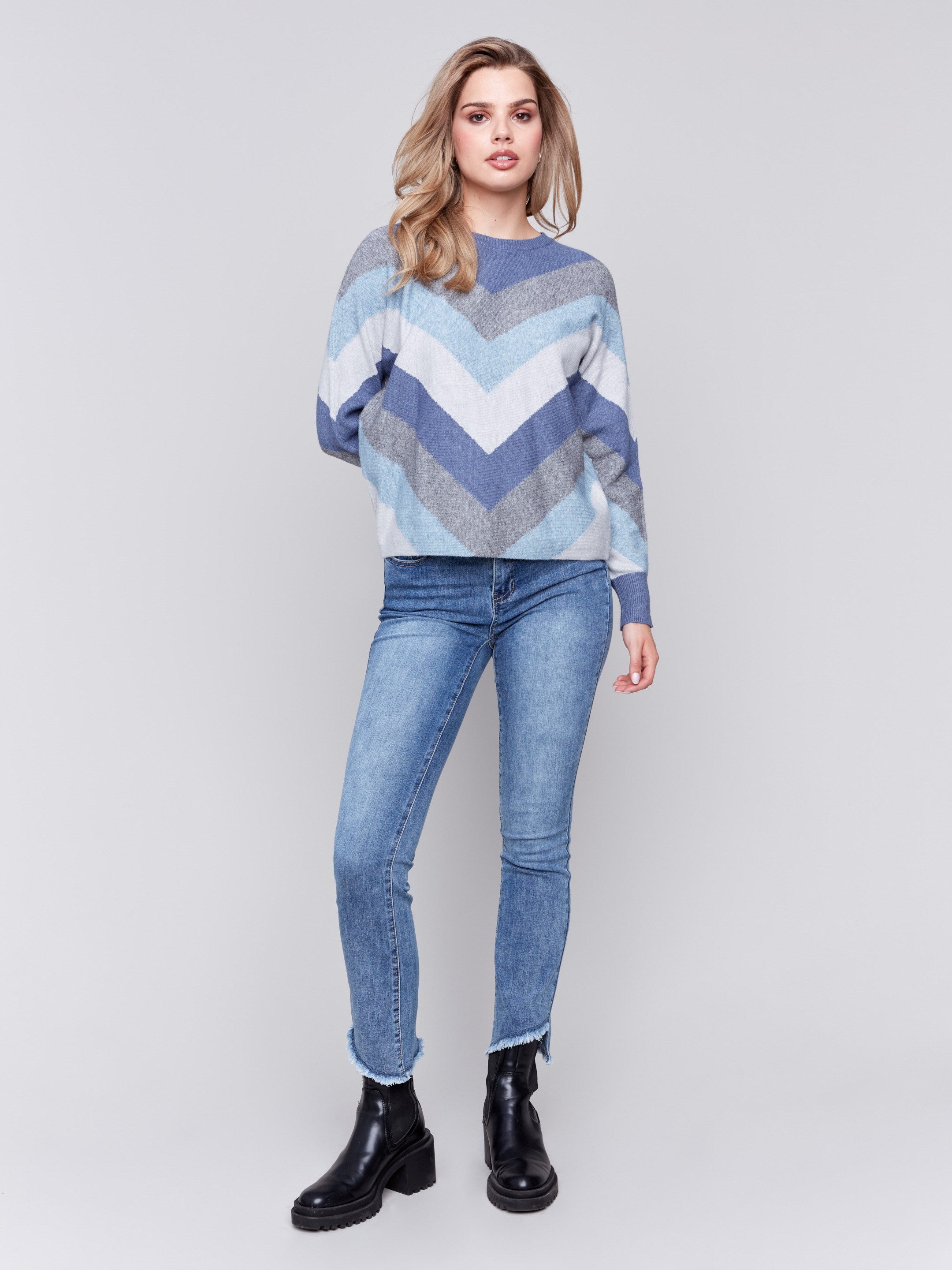 Denim-colored long-sleeve sweater with chevron stripes in blue, grey, and white. Crew neckline and ribbed cuffs by Charlie B.