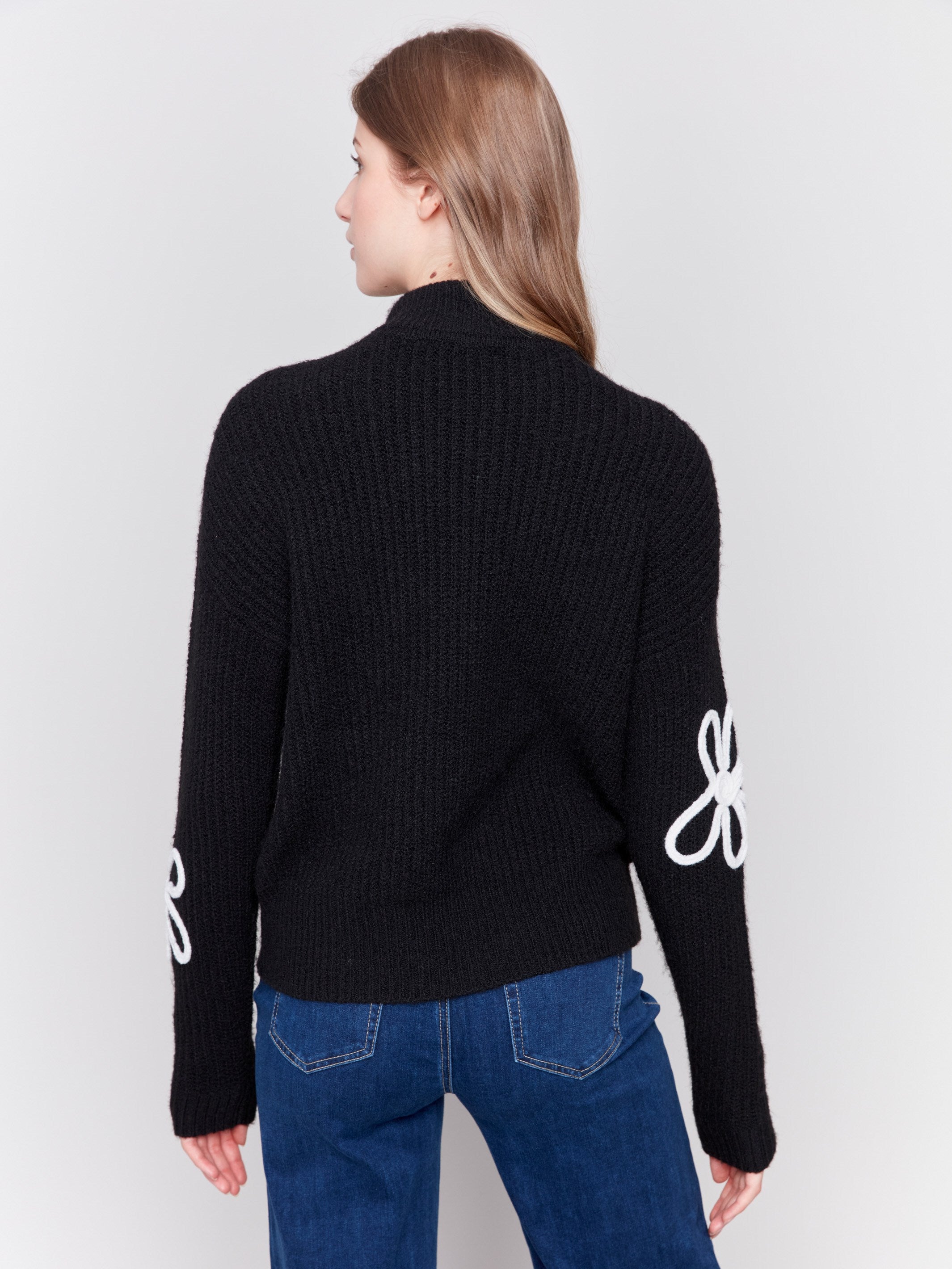 Black mock-neck sweater with white floral embroidery and ribbed texture by Charlie B.