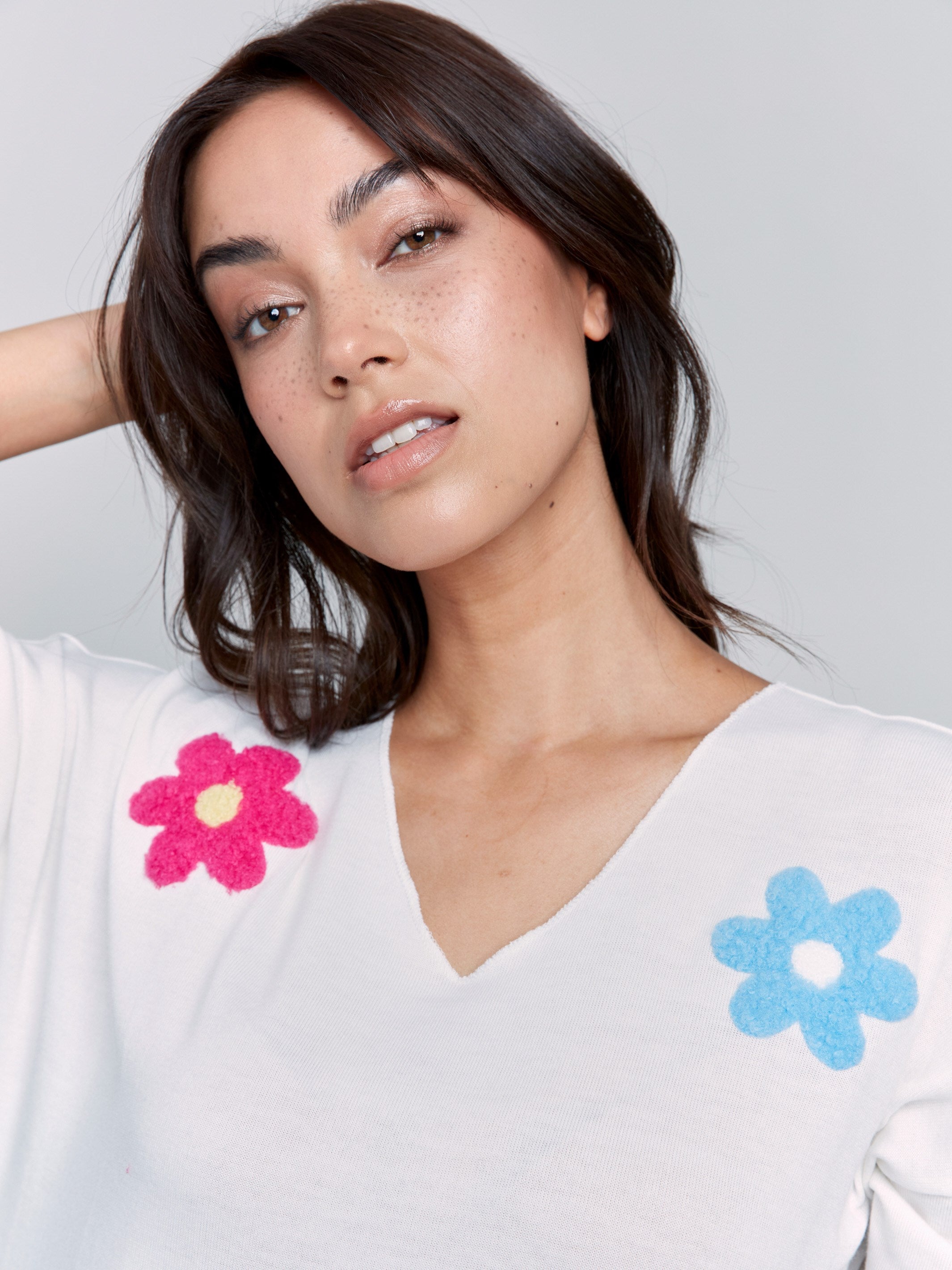 White V-neck knit top with colorful floral appliqués, featuring drop shoulders, by Charlie B.