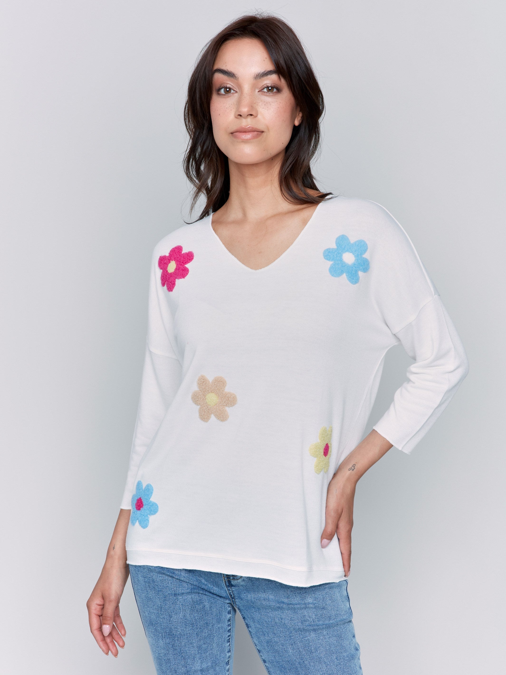 White V-neck knit top with colorful floral appliqués, featuring drop shoulders, by Charlie B.